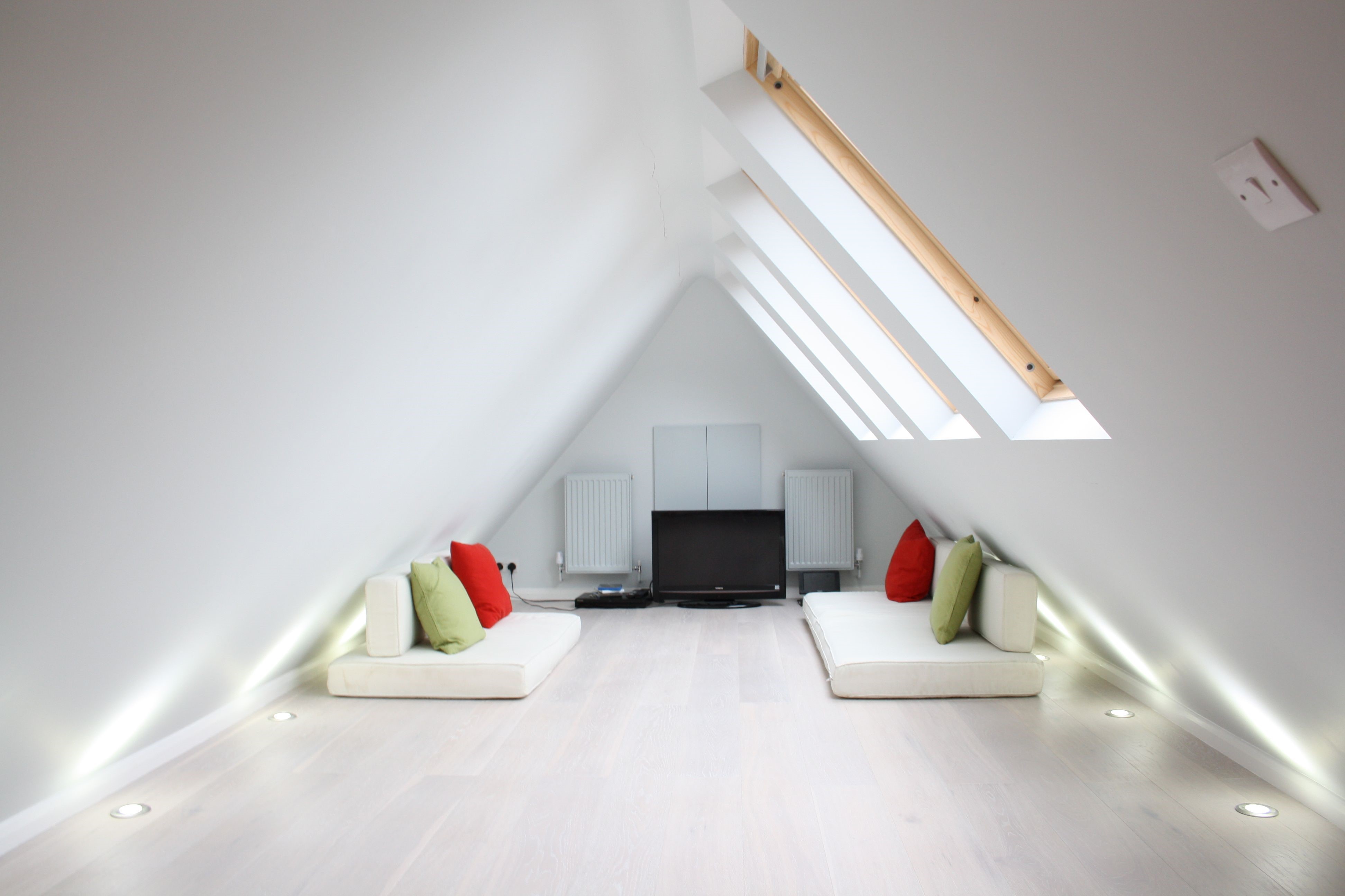 A minimalist loft conversion with floor cushions and a flat screen television